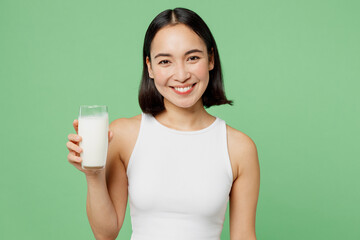 Young smiling happy fun woman wear white clothes hold in hand glass drink milk look camera isolated on plain pastel light green background. Proper nutrition healthy fast food unhealthy choice concept.