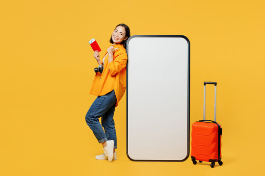 Young woman wear summer clothes stand near big huge blank screen mobile cell phone isolated on plain yellow background Tourist travel abroad in free time rest getaway. Air flight trip journey concept