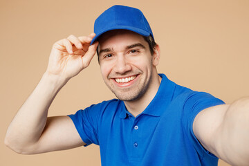 Close up delivery guy employee man wear blue t-shirt uniform workwear work as dealer courier touch cap do selfie shot pov on mobile cell phone isolated on plain light beige background Service concept