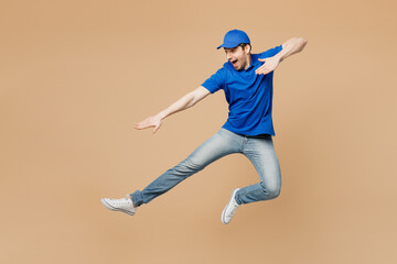 Fototapeta na wymiar Full body delivery guy employee man wear blue cap t-shirt uniform workwear work as dealer courier jump high pov fighting rejoicing fooling around isolated on plain beige background. Service concept.