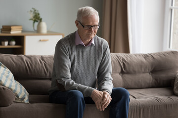 Sad depressed elderly man feeling lost, lonely at home, getting mental Alzheimer disease, memory loss, sitting on sofa at home looking into vacancy with bad thoughts, thinking on problems - obrazy, fototapety, plakaty