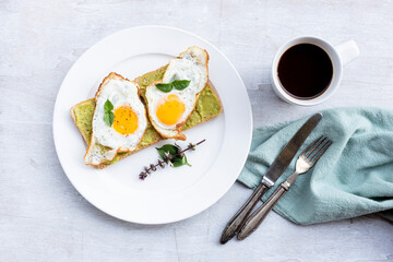 Breakfast food fried egg on bread avocado spread and coffee on white wood table.
