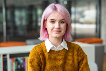 Female student with colored hair standing in coworking space with copy space. Portrait of young modern woman entrepreneur looking at a camera standing in creative office