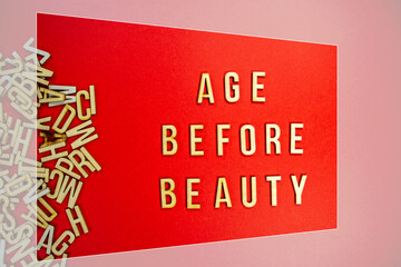 AGE BEFORE BEAUTY in wooden English words language capital letters spilling from a pile of letters on a red background - framed
