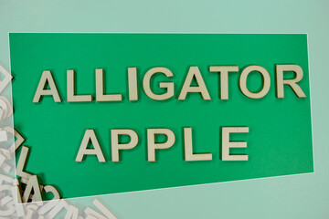 ALLIGATOR APPLE fruit in wooden English language capital letters spilling from a pile of letters on a green background framed