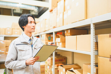 作業服を着て倉庫で在庫管理をする若いビジネスマン