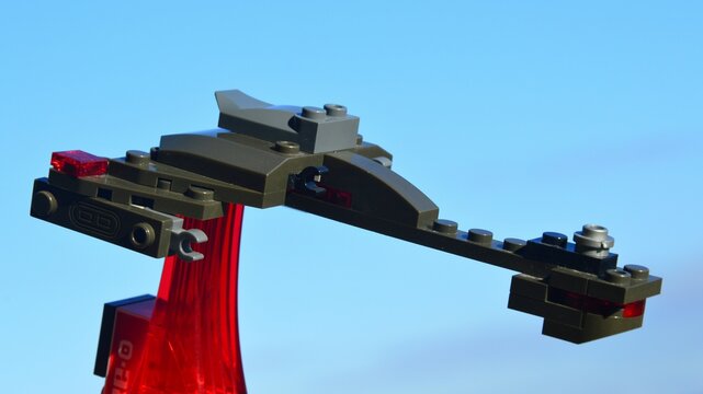 Miniature model of Klingon assault spaceship Bird Of Prey by KREO, made of brick compatible with LEGO, placed on red semi transparent stand, blue skies in backgroun