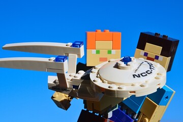 Fototapeta premium LEGO Minecraft figures of Steve and Alex examining KREO model of Star Trek spaceship USS Enterprise, blue morning winter skies, daylight sunshine. 
