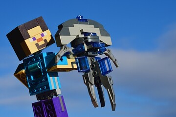 Fototapeta premium LEGO Minecraft large figure Steve adoring model of space ship Jellyfish from Star Trek movie series made by KREO (known as ship of Mr. Spock from planet Vulcan) in vertical position. Blue sky.