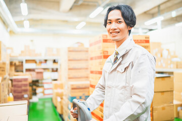 ハンドパレットで段ボールを運ぶ若い作業員