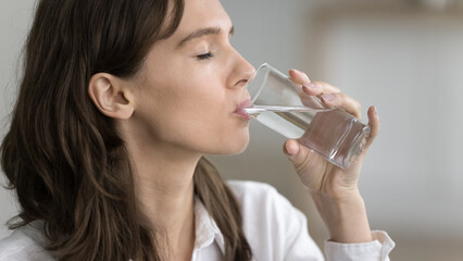 Pleased thirsty young woman drinking clear natural water from glass with closed eyes, recovering...