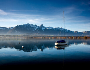 Single sail boat docked on a Swiss lake near the mountains