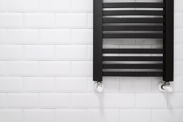 black heated towel rail in bathroom with white tile - obrazy, fototapety, plakaty