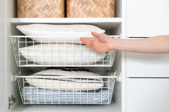 woman take bedclothes from metal white basket in wood wardrobe, closeup