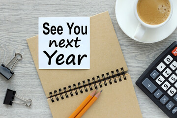 See you next year. wooden light background with a white sticker and a cup of coffee. text on paper. business concept.