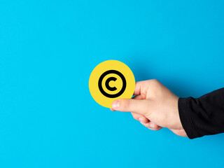 Copyright. Property rights and brand patent protection in business. Male hand holding a yellow badge sign with copyright symbol against blue background.