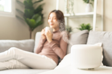 Obraz na płótnie Canvas Modern air humidifier during relax or rest, happy blurred asian young woman, girl enjoying aromatherapy steam scent from essential oil diffuser comfortable in living conditions room,apartment at home