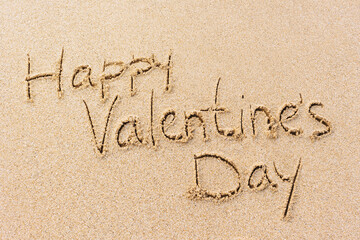 Happy Valentine's Day written on sand, greeting card design. Textured beach background.