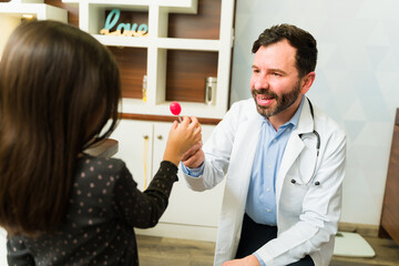 Cheerful pediatrician giving candy to a little patient
