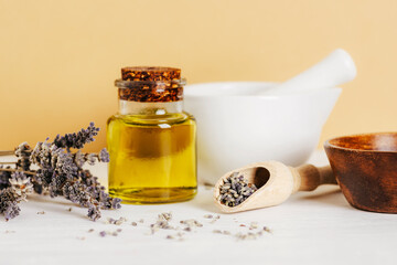 Natural cosmetic oil, white ceramic mortar and pestle and lavender dried flowers on white table. Natural cosmetics, skincare, aromatherapy and beauty products. Closeup