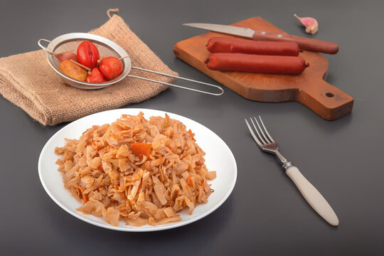 Stewed cabbage - bigos in a white porcelain plate against the background of smoked sausages and pickled vegetables