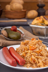 Braised cabbage - bigos and smoked sausages in a white porcelain plate against the background of baked potatoes and pickled vegetables. Close-up