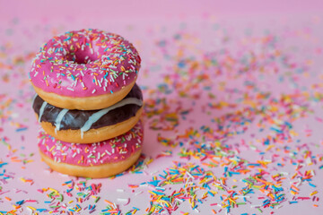 Delicious dessert. Pink, white and chocolate donuts with multicolored sprinkles on a pink background of Sweets. Confectionery products.