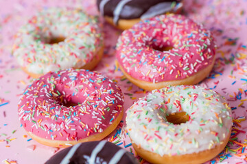 Delicious dessert. Pink, white and chocolate donuts with multicolored sprinkles on a pink background of Sweets. Confectionery products.