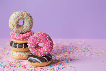 Delicious dessert. Pink, chocolate and white donuts with multicolored sprinkles on a purple...