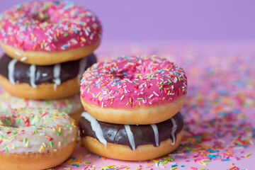 Delicious dessert. Pink, chocolate and white donuts with multicolored sprinkles on a purple background of Sweets. Confectionery products.