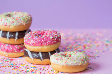 Delicious dessert. Pink, chocolate and white donuts with multicolored sprinkles on a purple background of Sweets. Confectionery products.