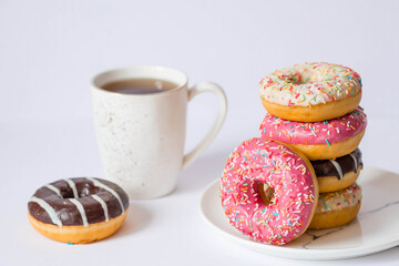 Delicious dessert. Pink, white and chocolate donuts with multicolored sprinkles, a cup of black coffee or tea. Sweets.