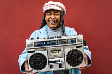 Happy trendy senior African woman having fun listening to music with vintage boombox stereo
