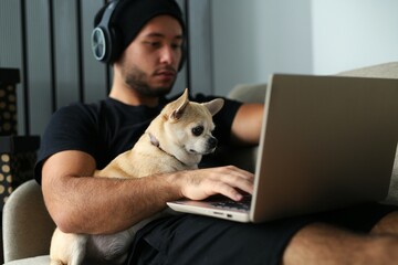 A young, stylish guy in black clothes is at home with his dog. A Chihuahua dog and a guy watch a...