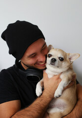stylish guy, teenager, dressed in black clothes, black hat. the guy is at home with his chihuahua dog, friends hugging, playing, spending time together, the dog is the guy's best friend. comfortable 