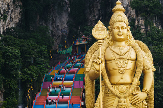 Close up shot of the largest Lord Murugan statue in malaysia with Batu caves colorful staircase background.