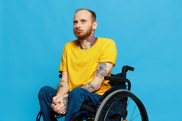 a man sits in a wheelchair in a t-shirt on a blue background in the studio, the concept of a free barrier-free environment for people with disabilities