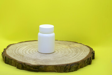 One white plastic medical container on wooden board on yellow background, mockup. Blank Medicine bottle. Pharmacy business and treatment concept. Close-up. Selective focus.