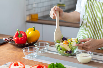 young woman is making salad from vegetables she has prepared on table in her home kitchen to get salad that is clean and safe because ingredients are carefully selected. healthy food preparation ideas