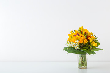 Beautiful fresh yellow freesia flower bouquet on white table at light gray wall background. Closeup. Empty place for inspirational text, lovely quote or positive sayings. Front view.