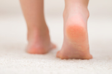 Little child feet on light soft carpet background. Barefoot step closeup. Back view. Showing heel.