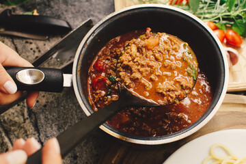 A kitchen ladle scooping bolognese sauce out of a pan