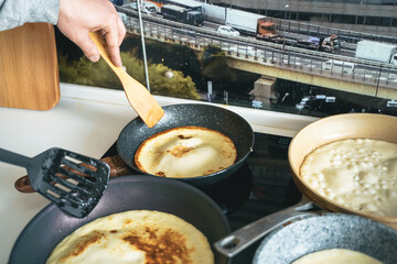 Russia Moscow 14.03.2021 Cooking many big tasty pancakes Lot of pans,oil,pancake dough.Russian traditional national festival winter Maslenitsa holiday week,shrovetide. Man, father cook.Family holiday