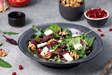 Salad mix with fresh spinach, walnuts, pomegranate and white cheese on a stone table.