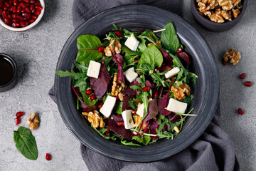 Salad mix with fresh spinach, walnuts, pomegranate and white cheese on a stone table. View from above.