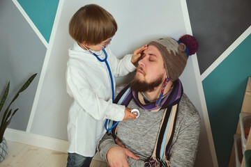 Fototapeta premium Father and child playing clinic and doctor, little boy in medical gown with stethoscope treats dad