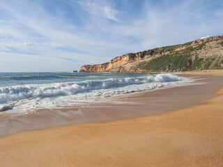 Atlantic ocean and sandy beach. Panoramic view with large, powerful wave in beautiful Silver Coast. Famous Nazaré Lighthouse or Farol on the steep cliff in the distance. Popular surf route in Portugal