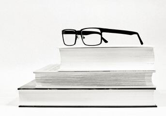 Drei dicke Bücher und eine Brille als Sehhilfe als Schwarzweißbild