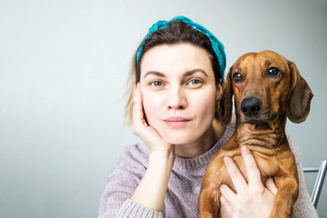 A portrait of a young, happy woman with a dachshund dog in her arms looking at the camera.