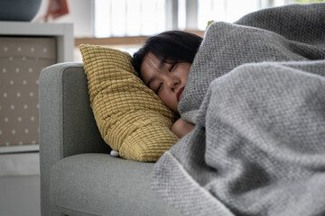 Sick Asian woman sleeping resting on sofa under blanket at home, recovering from flu. Sleepy weak...